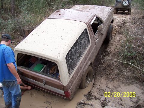 1987 Ford Bronco - A 1987 Ford Bronco is stuck deep in mud on a trail, with another vehicle visible in the background.