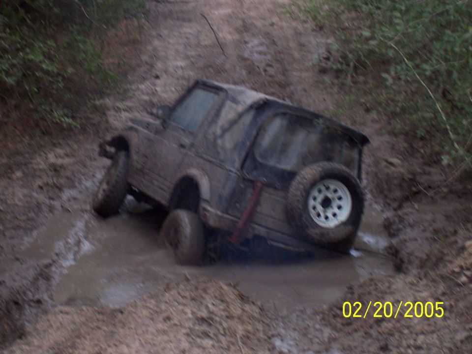 Muddy off-road vehicle stuck in a deep mud puddle on a dirt track