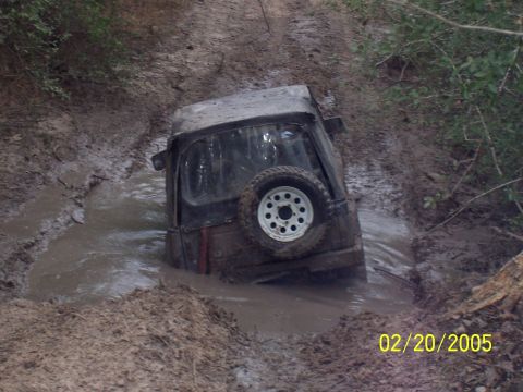 1987 Ford Bronco - This vehicle is deeply submerged in mud, with only the top and rear visible.