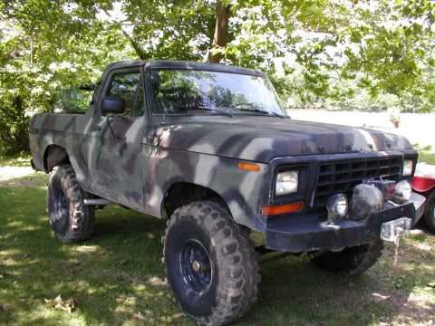1979 Ford Bronco - This pickup truck, likely a 1979 Ford Bronco, is covered in camouflage paint and sits on a grassy area.