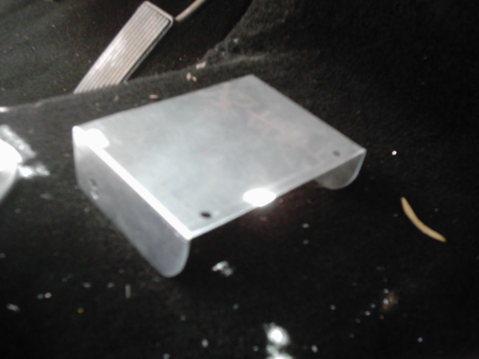 Metal bracket on dark carpet near a gas pedal
