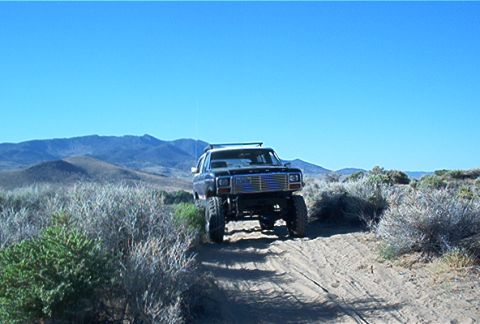 1986 Ford Bronco - A lifted black Ford Bronco navigates a dusty trail under a clear blue sky.