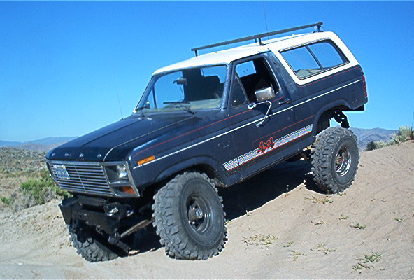 Dark blue Ford Bronco with white top and off-road tires on a dirt hill