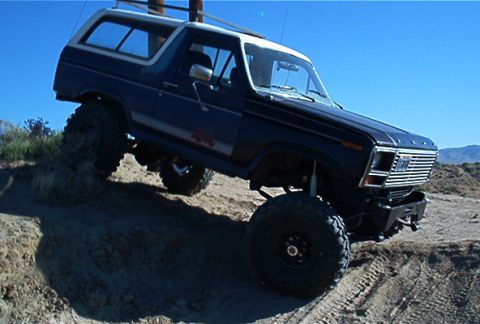 1986 Ford Bronco - This lifted 1980s Ford Bronco navigates a steep dirt incline under a clear blue sky.