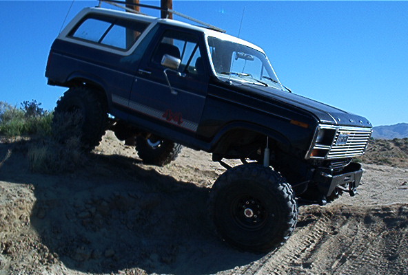 Dark blue 1980s Ford Bronco with off-road tires climbing a dirt hill