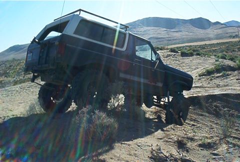 1986 Ford Bronco - This lifted Ford Bronco navigates a steep, dusty incline under a clear blue sky.