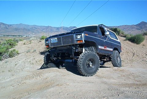 1986 Ford Bronco - This lifted 1986 Ford Bronco navigates a sandy hill under a clear blue sky.