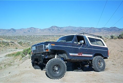 1986 Ford Bronco - Ford Bronco with lifted suspension and large tires on a dusty, off-road path.