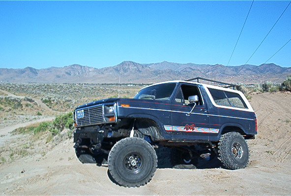 Dark blue Ford Bronco with white roof and 4x4 decals on a dirt trail
