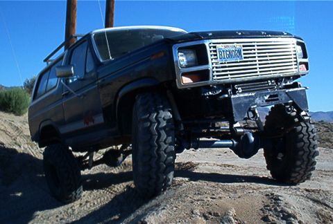 1986 Ford Bronco - This modified 1986 Ford Bronco is captured in a three-quarter front view, its lifted suspension and off-road tires on a dusty incline.