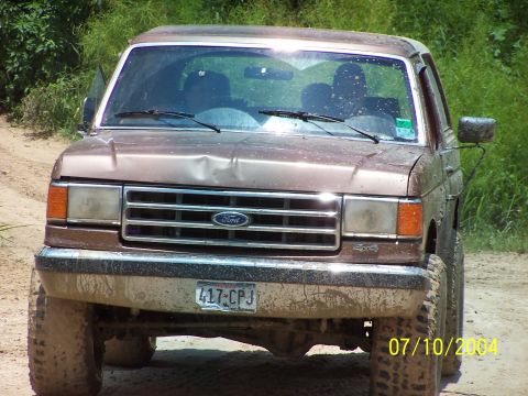 1987 Ford Bronco - Muddy 1987 Ford Bronco seen from the front, showing a dented hood and license plate 417-CPJ.