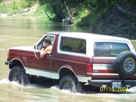 1987 Ford Bronco - A 1987 Ford Bronco navigates through a river, kicking up water as it goes.
