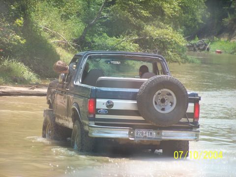 1987 Ford Bronco - 1987 Ford Bronco navigating a water crossing with two people inside.