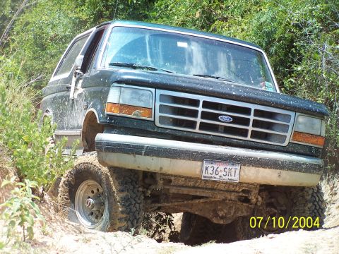 1987 Ford Bronco - Ford Bronco navigating a rough, off-road trail with dense foliage.