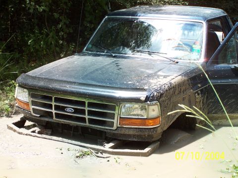 1987 Ford Bronco - This Ford truck appears to be stuck in a muddy area, with its front end partially submerged.