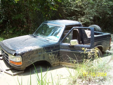 1987 Ford Bronco - A black Ford Bronco is stuck in the mud with its driver's door open.