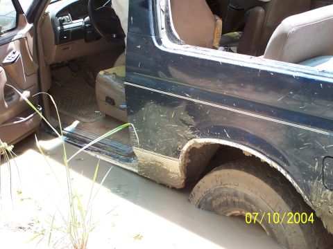1987 Ford Bronco - The interior of a Ford Bronco is visible with the driver's side door open, stuck in muddy terrain.
