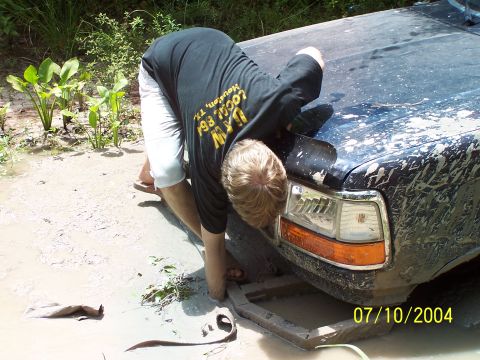 1987 Ford Bronco - A man inspects the front of a muddy 1992 Ford F-150 truck.