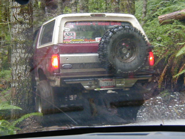 1992 Ford Bronco with spare tire on back, driving off-road near trees