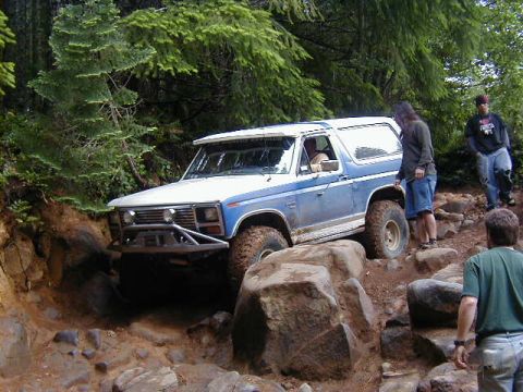 1994 Ford Explorer - A blue and white SUV tackles a challenging rocky off-road course with people observing.