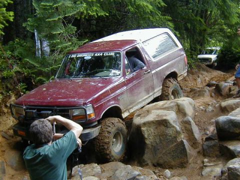 1994 Ford Explorer - A maroon Ford Bronco navigates a difficult rocky terrain on an off-road trail, with a second vehicle visible in the background.