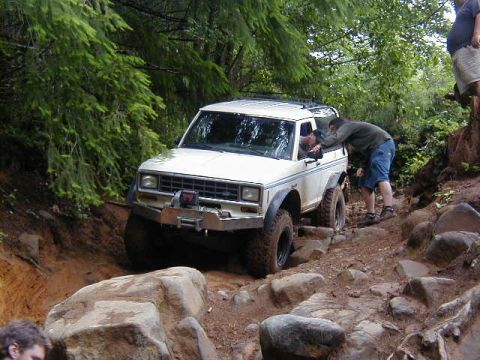 1994 Ford Explorer - White off-road SUV navigates a challenging rocky trail, with a person leaning into the driver's side window.