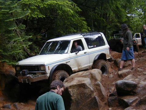 1994 Ford Explorer - An off-road vehicle navigates a challenging rocky trail with trees and other vehicles in the background.