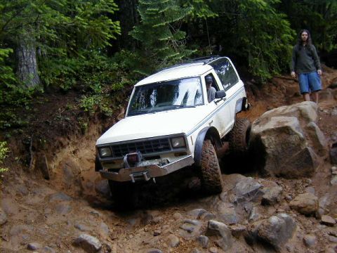 1994 Ford Explorer - A white 1984 Jeep Cherokee XJ tackles a challenging rocky incline on a wooded trail.