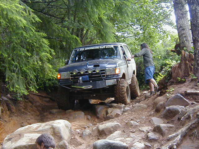 Dark blue Ford Bronco off-roading on a rocky, wooded trail