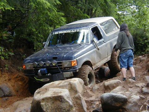 1994 Ford Explorer - This dark blue SUV, likely a 1992 Ford Bronco, tackles a challenging rocky off-road course with a person observing nearby.