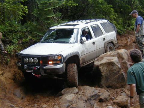 1994 Ford Explorer - A white SUV is carefully driven over large rocks on a challenging off-road trail surrounded by trees.