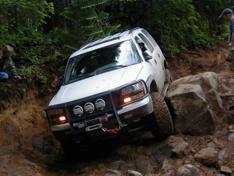 1994 Ford Explorer - A white SUV tackles a challenging off-road trail with large rocks and steep inclines.