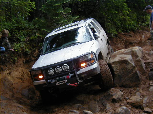 White SUV with a winch and auxiliary lights navigating a steep, rocky incline