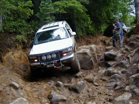 1994 Ford Explorer - A white SUV carefully maneuvers through a challenging off-road course with steep inclines and large rocks.