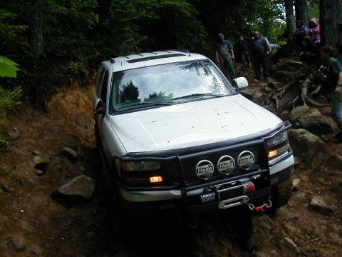 1994 Ford Explorer - White SUV with winch and Hella lights navigates a rocky, wooded trail.
