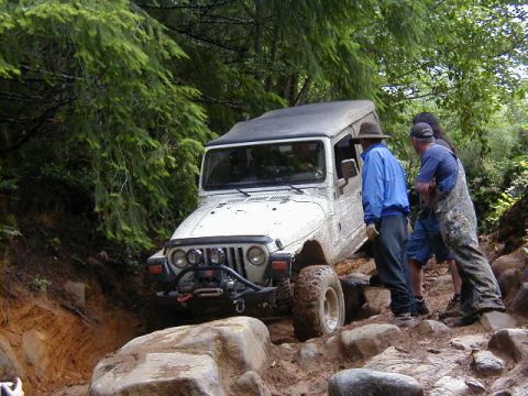 1994 Ford Explorer - A white Jeep Wrangler tackles a challenging rocky trail, with onlookers observing the off-road adventure.