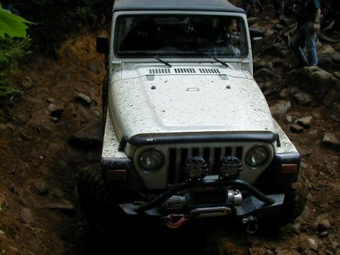 1994 Ford Explorer - A white Jeep Wrangler navigates a challenging off-road path with steep inclines and loose terrain.
