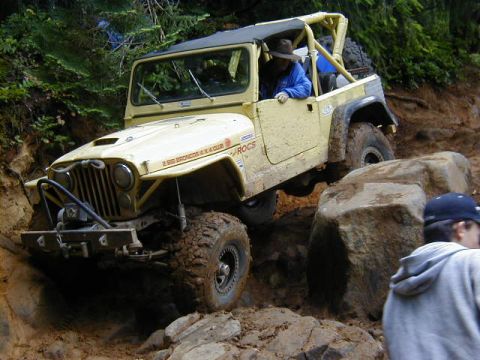 1994 Ford Explorer - This off-road vehicle navigates a challenging muddy and rocky terrain, with visible club affiliation text on its fender.