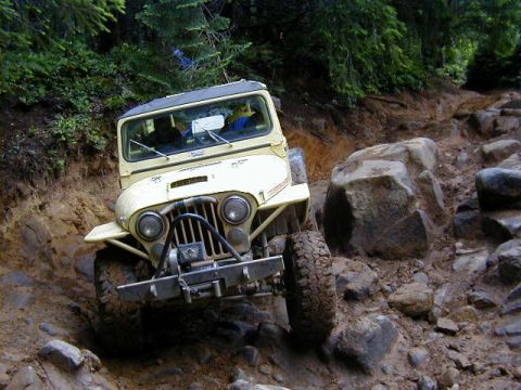 1994 Ford Explorer - This Jeep CJ-7 is tackling a challenging rocky and muddy trail in a wooded area.