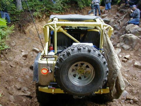 1994 Ford Explorer - A modified off-road vehicle is shown from the rear, climbing a challenging, rocky incline with spectators on the side.