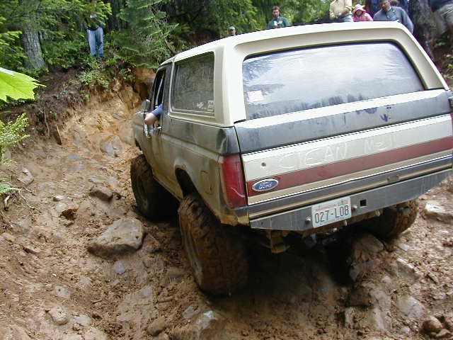 Rear view of a tan and gray Ford Bronco on a muddy trail