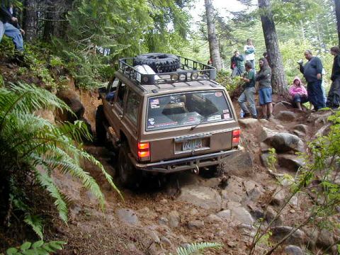 1994 Ford Explorer - A Jeep navigates a challenging off-road course, with spectators observing from the side.