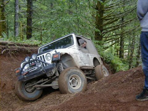 1994 Ford Explorer - A white Jeep Wrangler navigates a challenging off-road trail through a wooded area.