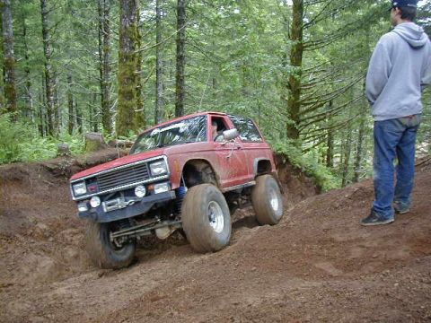 1994 Ford Explorer - A red SUV navigates a steep dirt incline in a wooded area, with a bystander observing the off-road action.