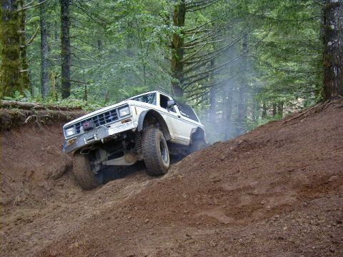 1994 Ford Explorer - A white 1989 Ford Bronco navigates a challenging dirt incline, kicking up dust and smoke.