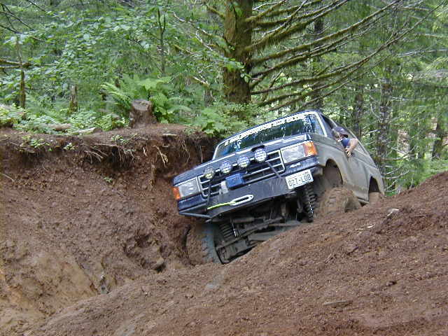 off-road SUV with winch and extra lights climbing steep dirt hill in woods