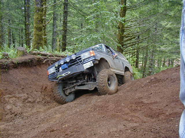 Dark gray Ford Bronco climbing a dirt hill, front-left tire off the ground