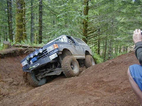 1994 Ford Explorer - Off-road SUV with aftermarket lights navigates a challenging dirt trail in a wooded area.