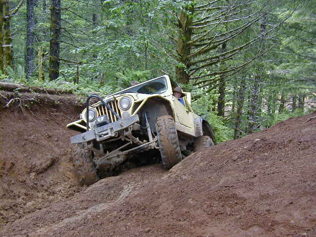 Yellow Jeep CJ-7 going down a steep dirt hill in a forest