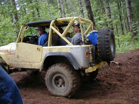 1994 Ford Explorer - A yellow off-road jeep navigates a muddy trail through a forest.